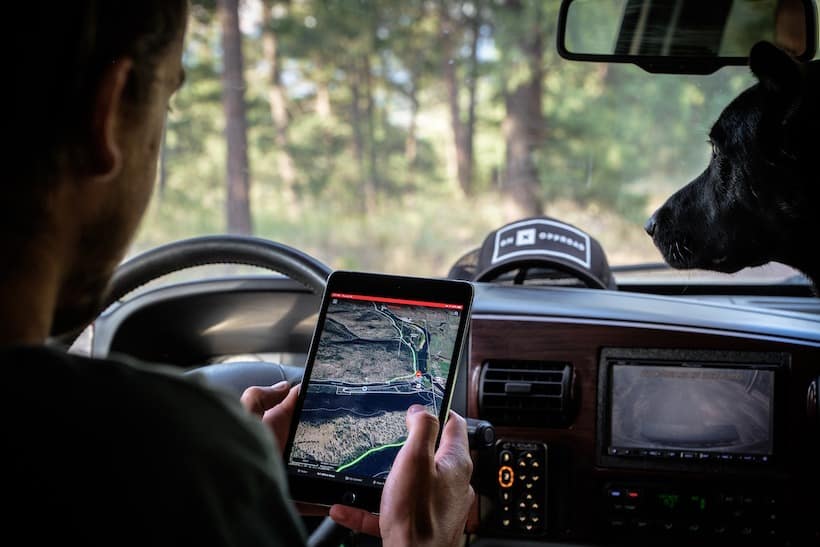 A person in an off-road vehicle using a smartphone navigation app with their dog companion, demonstrating how to get started with the Off Road Treasure Quest.