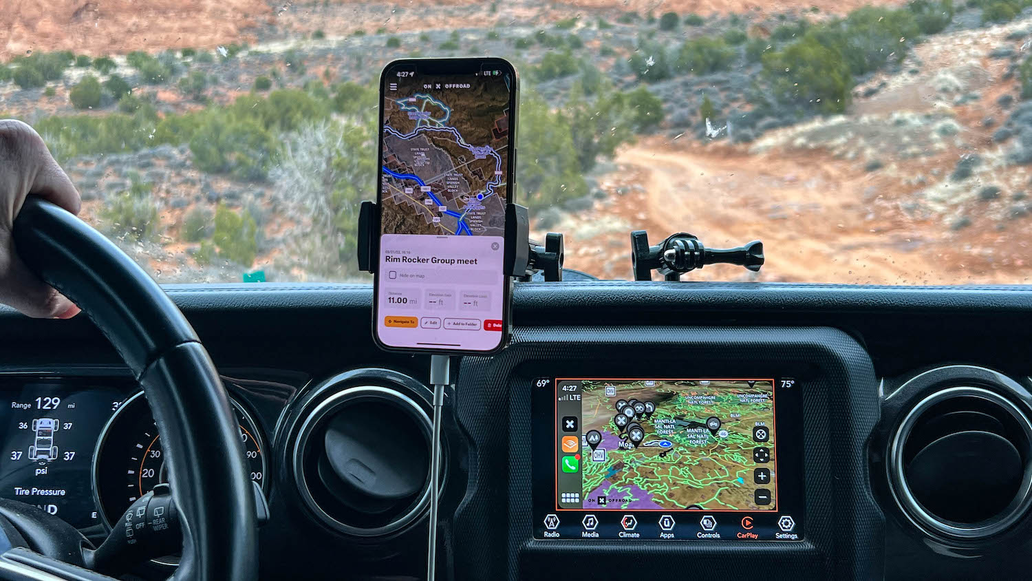 Interior view of an off-road vehicle showing both smartphone and dashboard navigation systems displaying detailed topographic maps and waypoints, demonstrating the modern technology used to decipher clues and navigate to treasure locations.