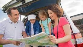 A multi-generational family gathered around the back of their SUV, collaboratively studying a map and planning their off-road adventure together.
