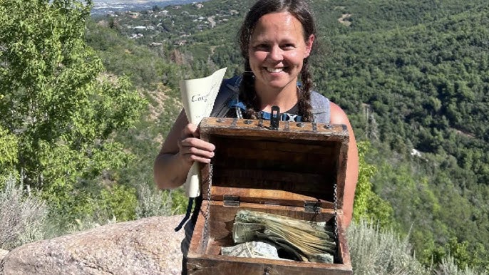 A woman outdoors holding a wooden treasure chest filled with cash, demonstrating prize redemption for Off Road Treasure Quest.