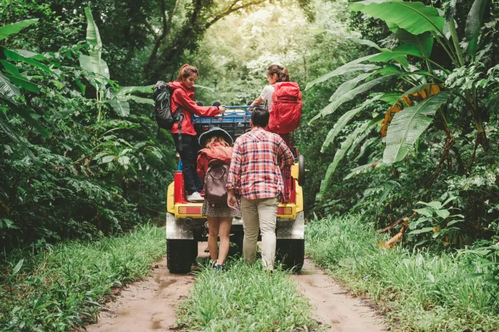 Friends hiking in a tropical forest, riding a jeep with backpacks, enjoying the adventure.